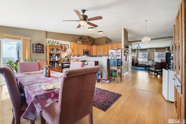 dining space with ceiling fan with notable chandelier, light wood-type flooring, and lofted ceiling