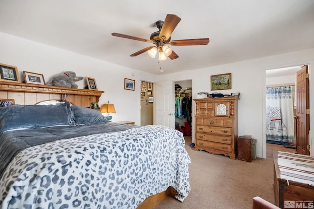 bedroom featuring a walk in closet, a closet, light carpet, and ceiling fan