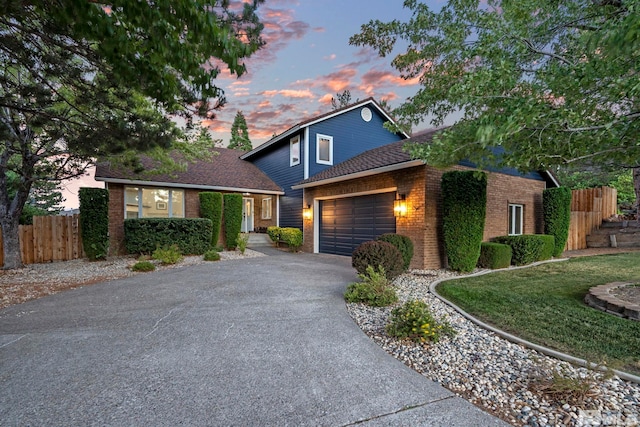 traditional home featuring aphalt driveway, brick siding, roof with shingles, fence, and a garage