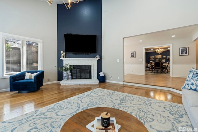 living area featuring wood-type flooring, a fireplace, a high ceiling, and an inviting chandelier