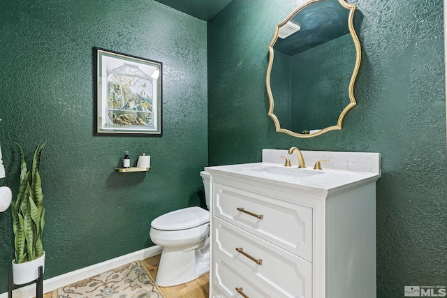 half bathroom with a textured wall, vanity, toilet, and wood finished floors