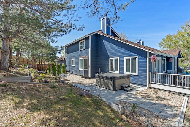 back of house featuring a hot tub, a vegetable garden, a chimney, fence, and a patio area
