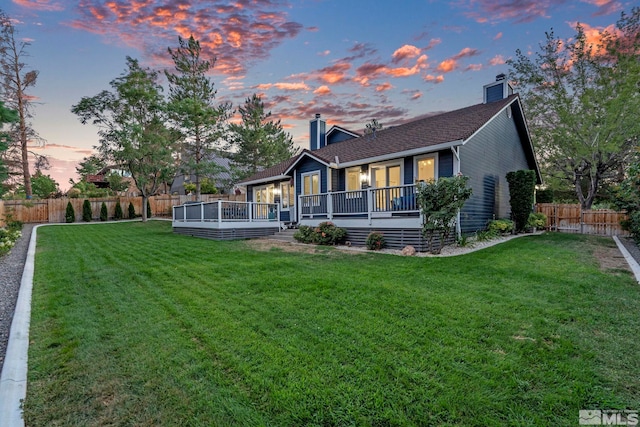 back of house at dusk featuring a chimney, fence, and a lawn