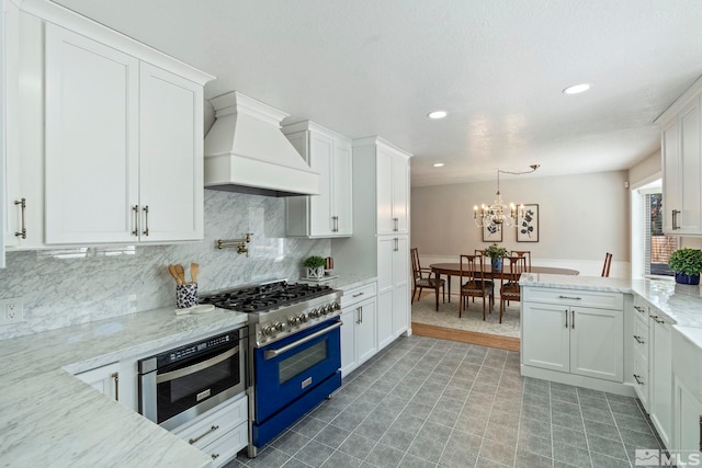 kitchen with premium range hood, white cabinetry, high end range, light stone countertops, and tasteful backsplash