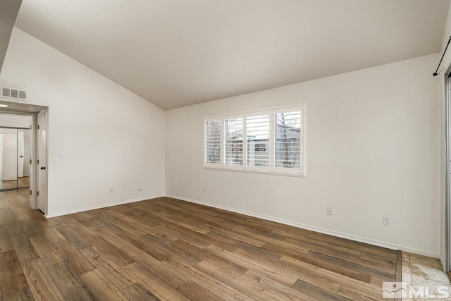 spare room featuring visible vents, vaulted ceiling, baseboards, and wood finished floors