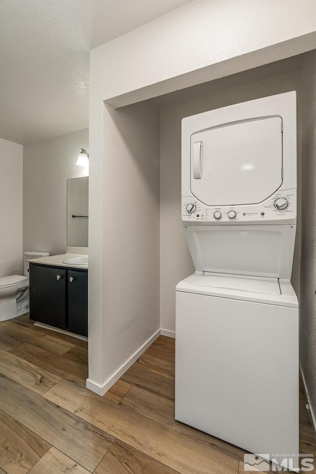 washroom with baseboards, a textured ceiling, stacked washing maching and dryer, and wood finished floors