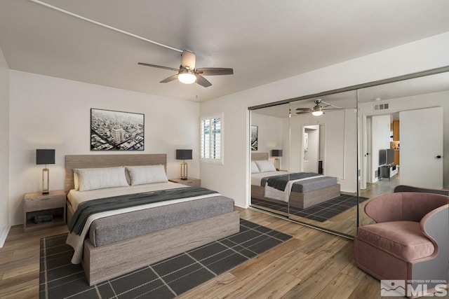 bedroom with baseboards, visible vents, ceiling fan, wood finished floors, and a closet