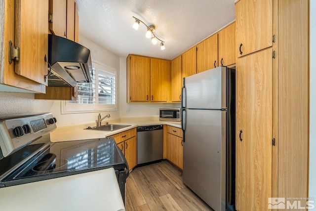 kitchen with stainless steel appliances, light wood-style floors, a sink, a textured ceiling, and ventilation hood