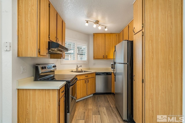 kitchen with appliances with stainless steel finishes, a sink, a textured ceiling, light wood-type flooring, and under cabinet range hood