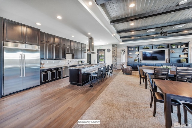 kitchen featuring open floor plan, appliances with stainless steel finishes, light wood-type flooring, beamed ceiling, and island exhaust hood