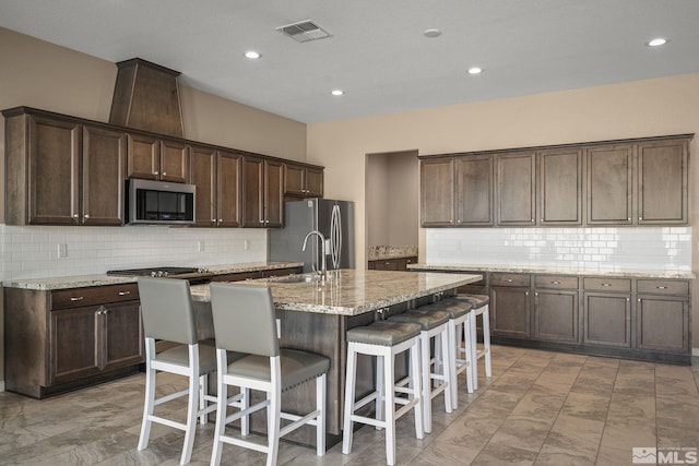 kitchen featuring a kitchen island with sink, dark brown cabinetry, visible vents, marble finish floor, and appliances with stainless steel finishes