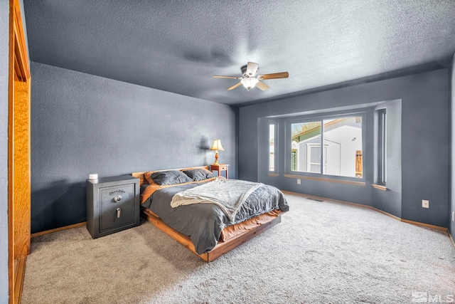 carpeted bedroom featuring a textured wall, a textured ceiling, baseboards, and ceiling fan