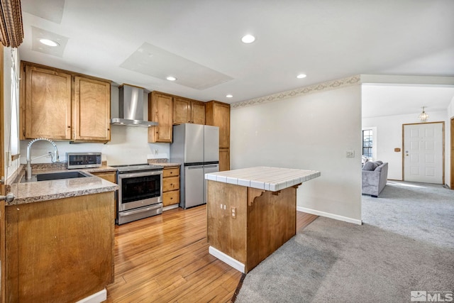 kitchen with stainless steel appliances, brown cabinetry, a sink, a kitchen island, and wall chimney exhaust hood