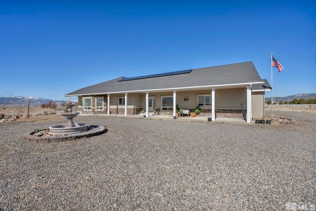 back of house with roof mounted solar panels, a mountain view, a patio, and stucco siding