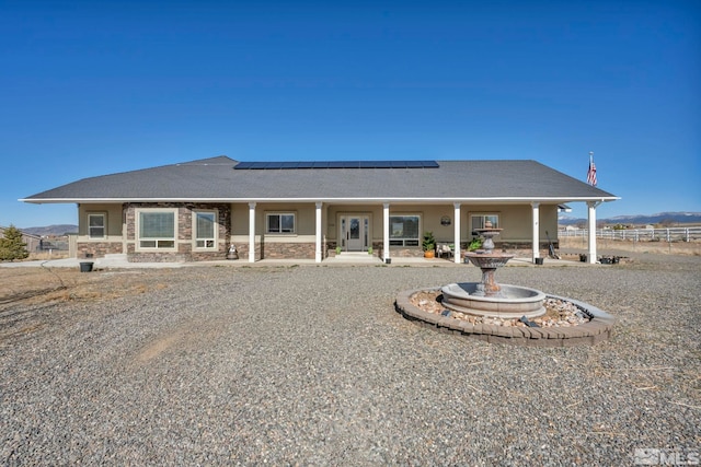 back of house featuring stone siding, fence, and solar panels