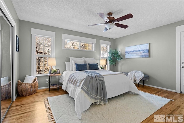 bedroom featuring baseboards, ceiling fan, wood finished floors, a textured ceiling, and a closet