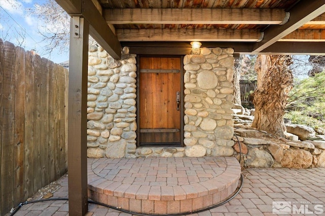 view of exterior entry featuring stone siding and fence