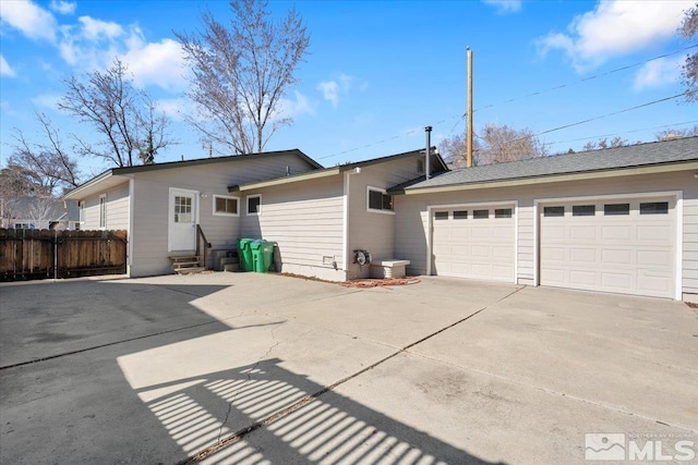 rear view of property with entry steps, concrete driveway, an attached garage, and fence