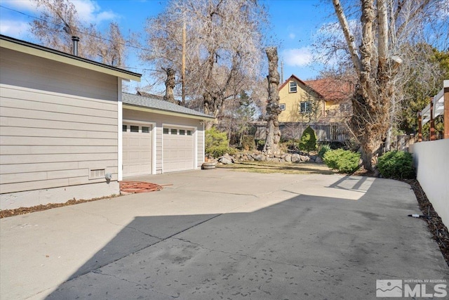 garage featuring concrete driveway and fence