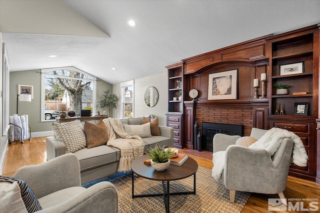 living area featuring a textured ceiling, a fireplace, baseboards, vaulted ceiling, and light wood-type flooring