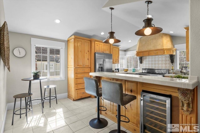 kitchen with wine cooler, stainless steel refrigerator with ice dispenser, tile counters, tasteful backsplash, and custom range hood