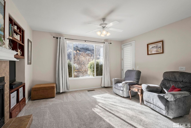 living area featuring a fireplace, carpet flooring, visible vents, baseboards, and a ceiling fan