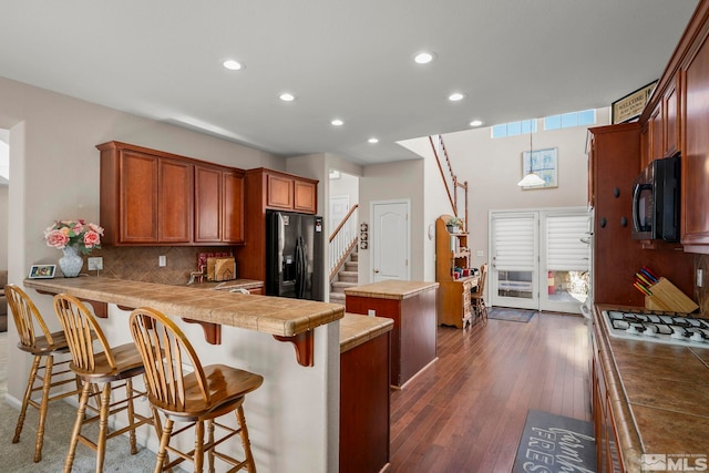 kitchen with a kitchen island, dark wood-type flooring, a peninsula, black appliances, and backsplash