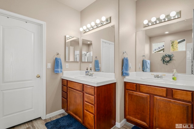 bathroom featuring baseboards, two vanities, a sink, and wood finished floors