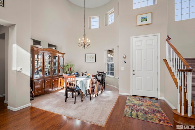 dining room with a chandelier, wood finished floors, a towering ceiling, baseboards, and stairs