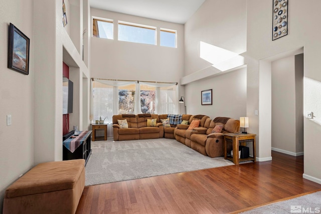 living area with a towering ceiling, baseboards, and wood finished floors