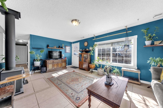 tiled living area featuring a wood stove, baseboards, visible vents, and a textured ceiling