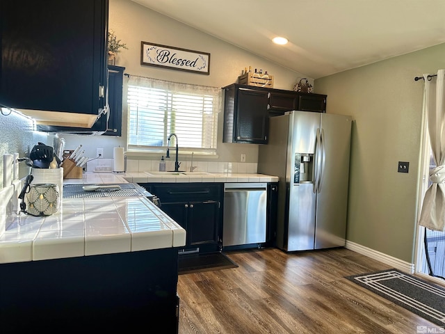 kitchen with lofted ceiling, tile counters, appliances with stainless steel finishes, and a sink