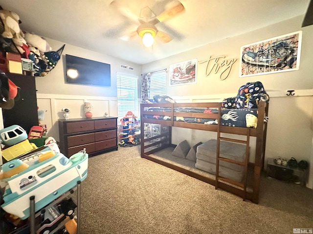 carpeted bedroom featuring a decorative wall, a wainscoted wall, and ceiling fan