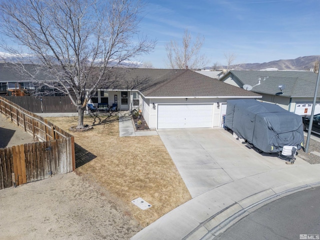 ranch-style home featuring fence, roof with shingles, concrete driveway, a garage, and a mountain view