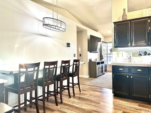 kitchen featuring tile countertops, baseboards, lofted ceiling, and light wood finished floors