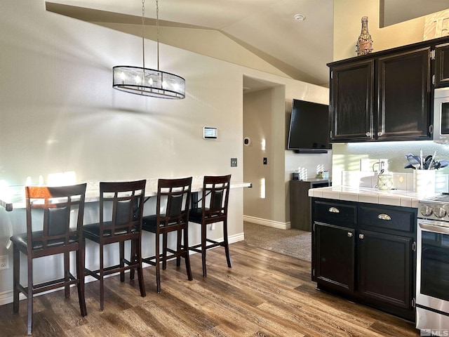 kitchen with tile counters, dark wood finished floors, lofted ceiling, dark cabinetry, and stainless steel appliances