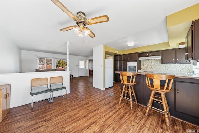 kitchen with white appliances, open floor plan, wood finished floors, dark brown cabinets, and under cabinet range hood