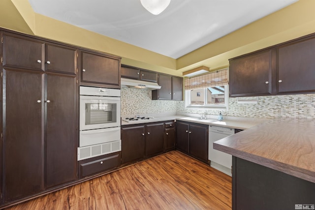 kitchen featuring a warming drawer, dark brown cabinets, wood finished floors, white appliances, and under cabinet range hood