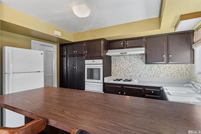 kitchen featuring under cabinet range hood, white appliances, a sink, dark brown cabinets, and a warming drawer