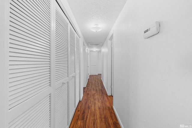 corridor with attic access, baseboards, dark wood-type flooring, and a textured ceiling