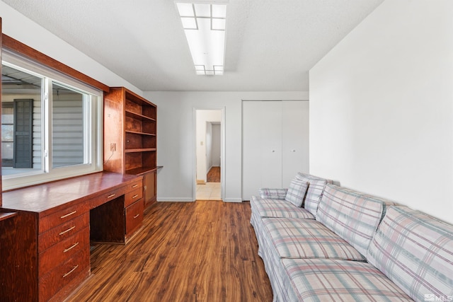 office with dark wood finished floors, built in desk, and baseboards