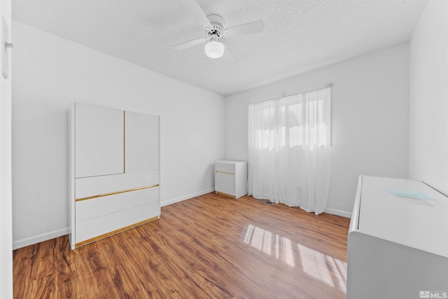 empty room featuring ceiling fan, a textured ceiling, baseboards, and wood finished floors