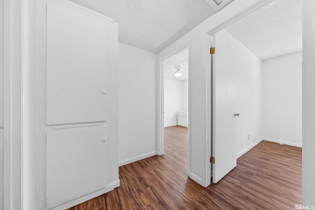 hall featuring a textured ceiling, baseboards, and wood finished floors