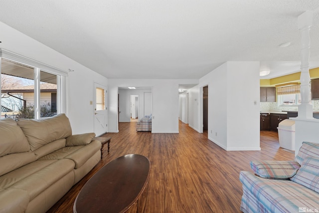 living room featuring ornate columns, baseboards, and wood finished floors