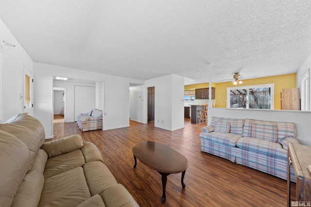 living area featuring baseboards, a textured ceiling, a ceiling fan, and wood finished floors