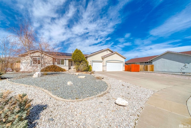 single story home with solar panels, concrete driveway, an attached garage, fence, and stucco siding