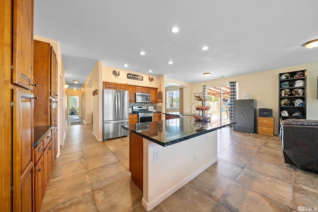 kitchen with arched walkways, dark countertops, appliances with stainless steel finishes, brown cabinets, and backsplash