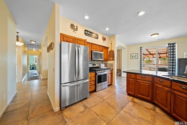 kitchen with decorative backsplash, dark countertops, brown cabinets, stainless steel appliances, and a sink