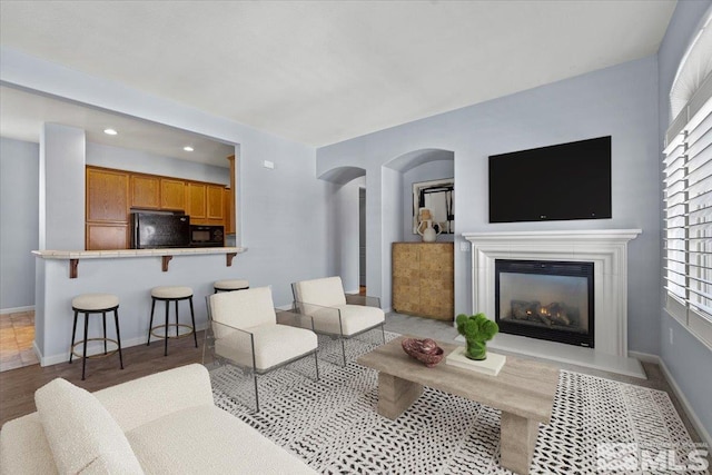 living area featuring baseboards, arched walkways, a glass covered fireplace, wood finished floors, and recessed lighting