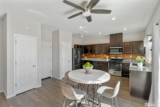 kitchen featuring dark brown cabinetry, appliances with stainless steel finishes, backsplash, wood finished floors, and a sink